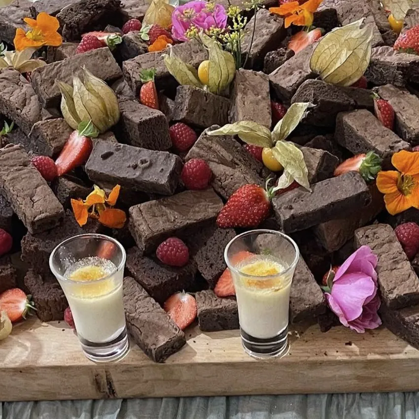 Platter of brownies with strawberries, raspberries, physalis, edible flowers, and two small dessert glasses