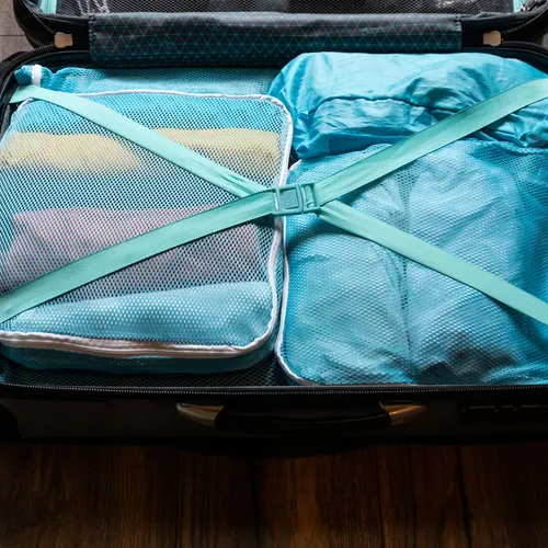 Suitcase packed with blue packing cubes and crossed straps