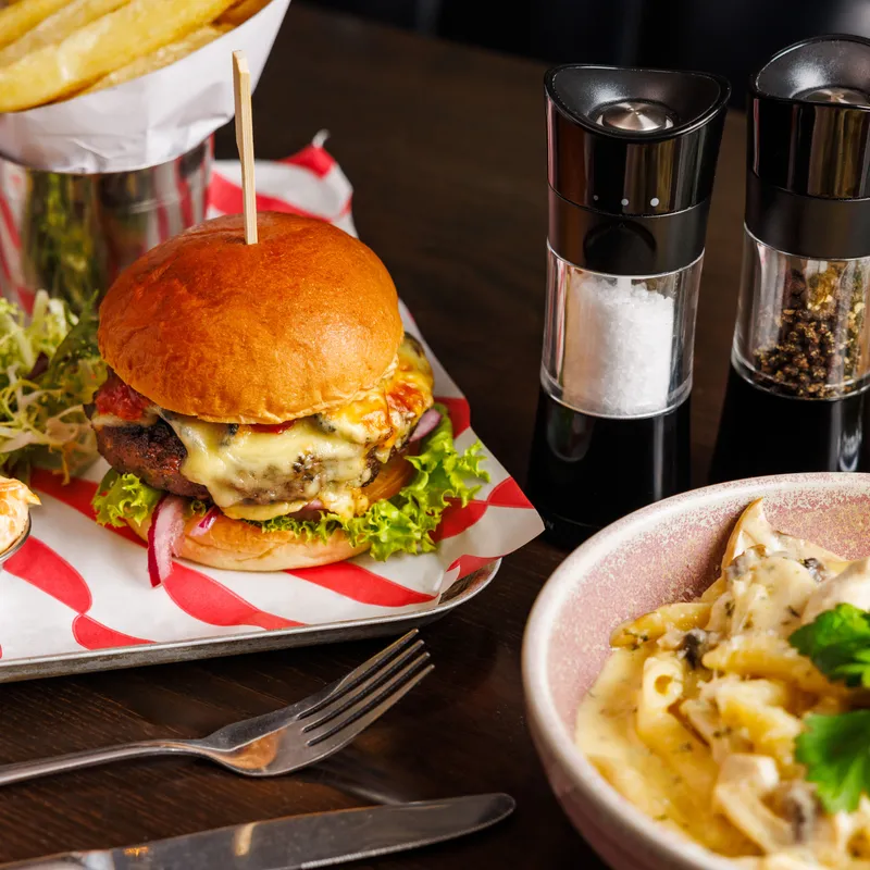 Cheeseburger with lettuce and red onion served with chips, salt and pepper grinders, and a bowl of creamy pasta.