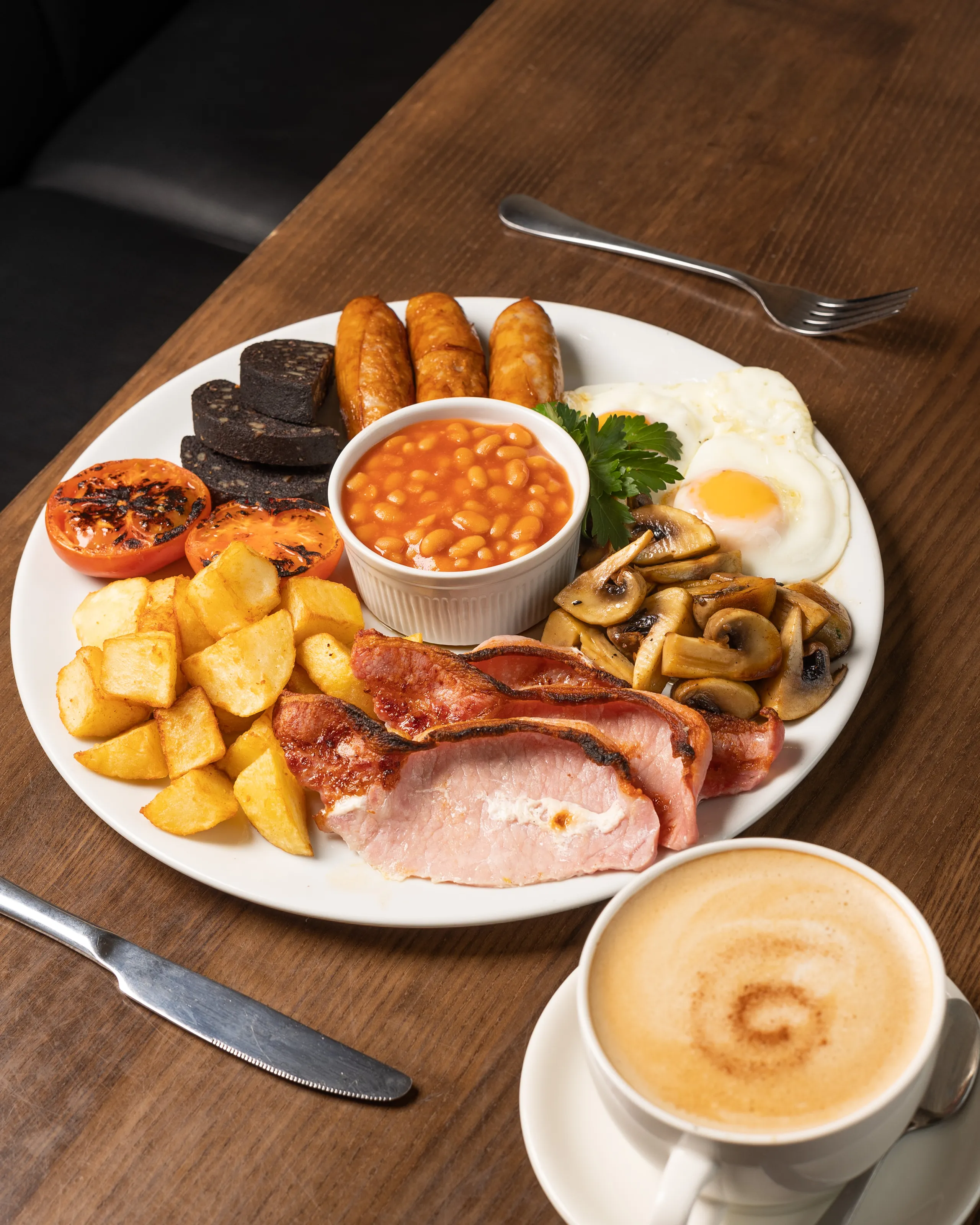 Full English breakfast with bacon, sausages, fried egg, black pudding, beans, mushrooms, grilled tomatoes, potatoes and coffee