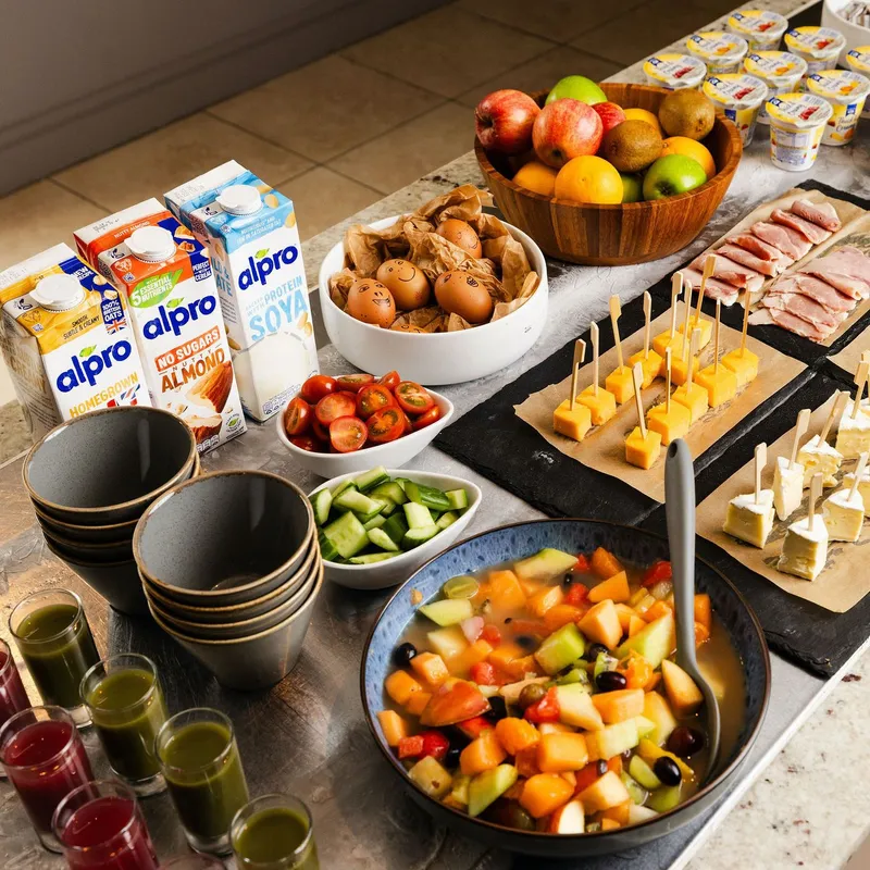 Hotel breakfast buffet with fresh fruit, cheeses, cold meats, dairy-free milk, yoghurt and juices.