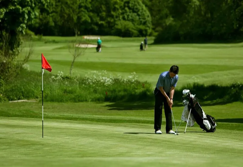 Golfer putting beside a red flag on a green golf course
