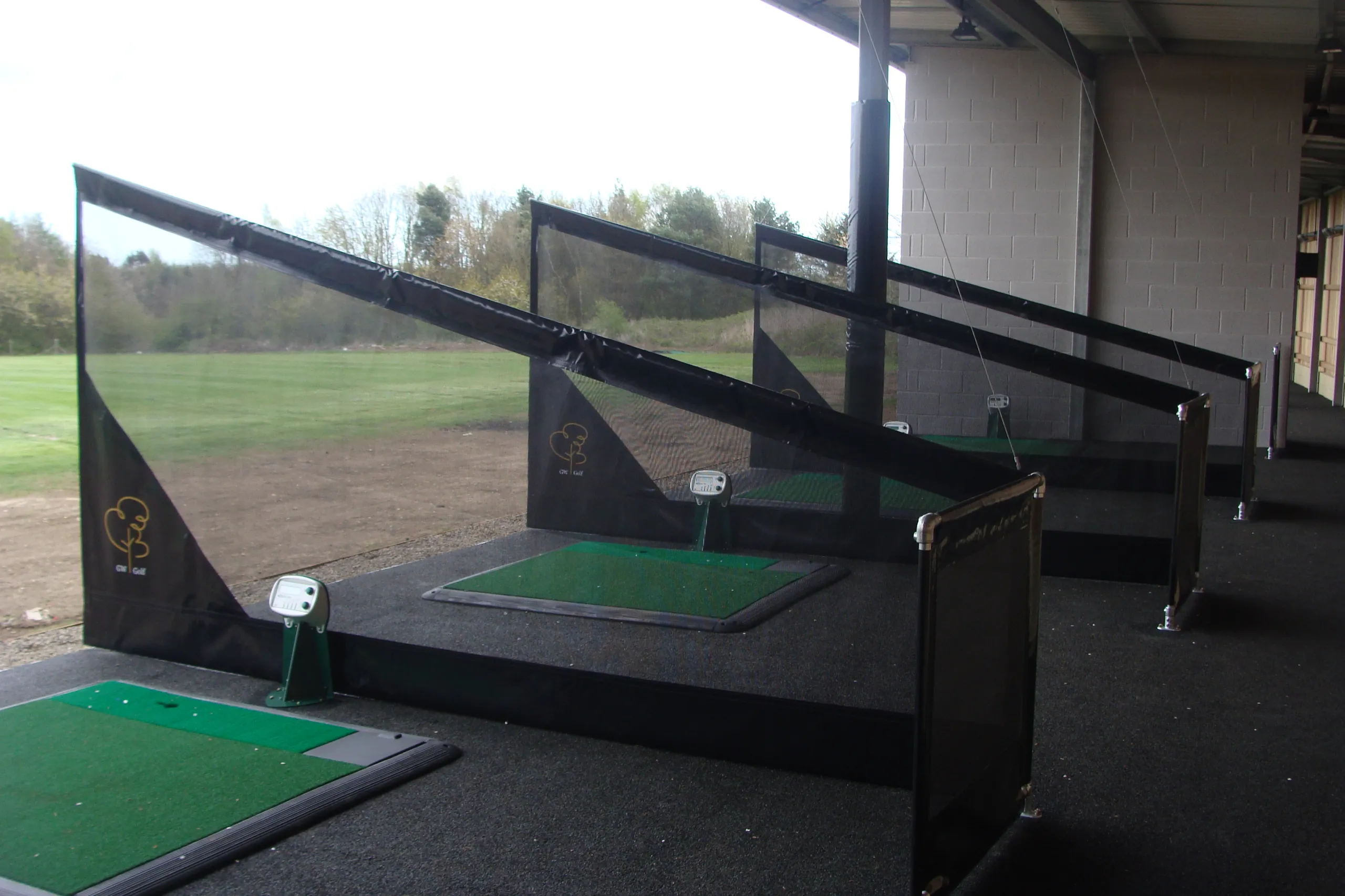 Covered golf driving range bays with green hitting mats and protective netting
