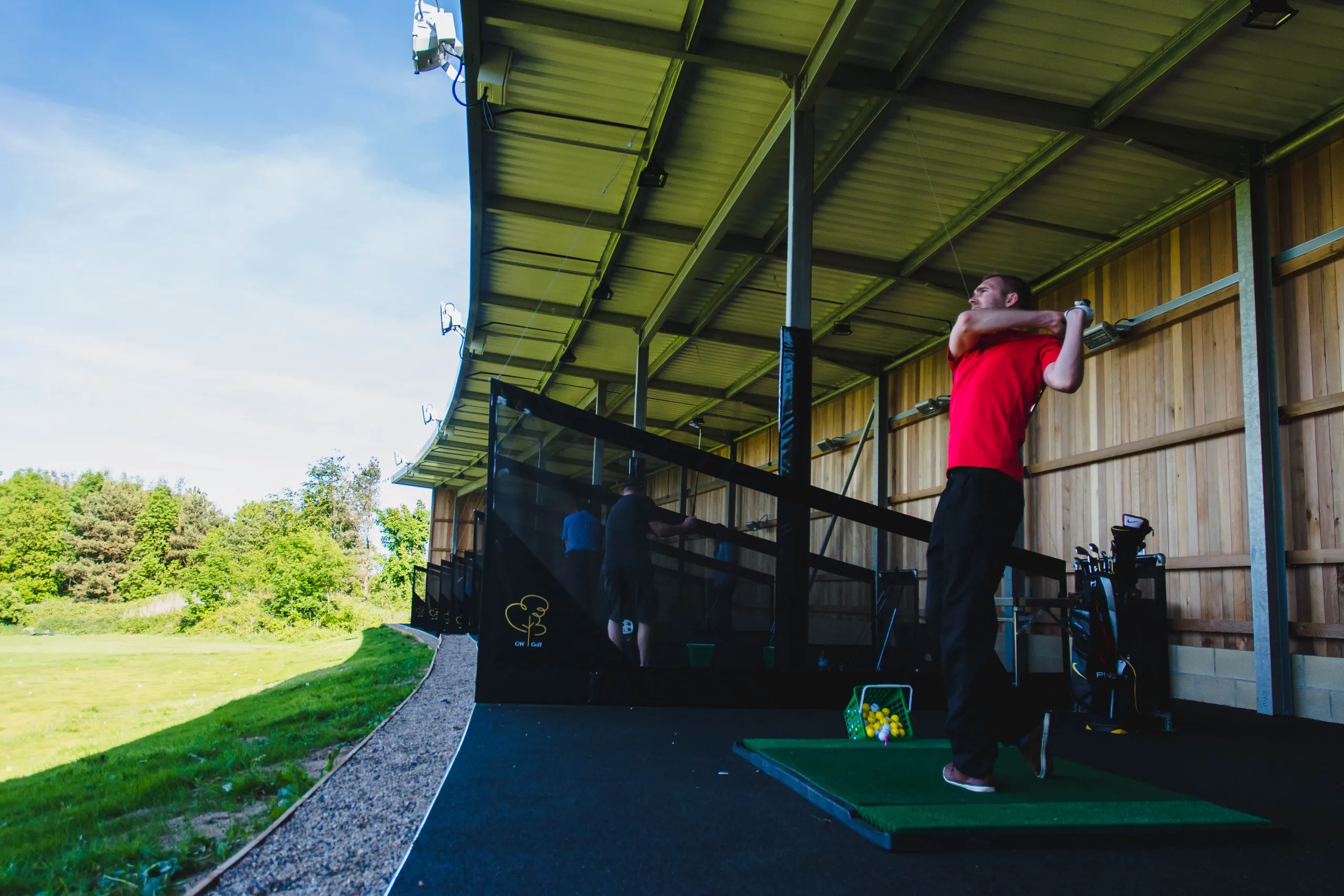 Golfer in a red shirt finishing a swing at a covered driving range