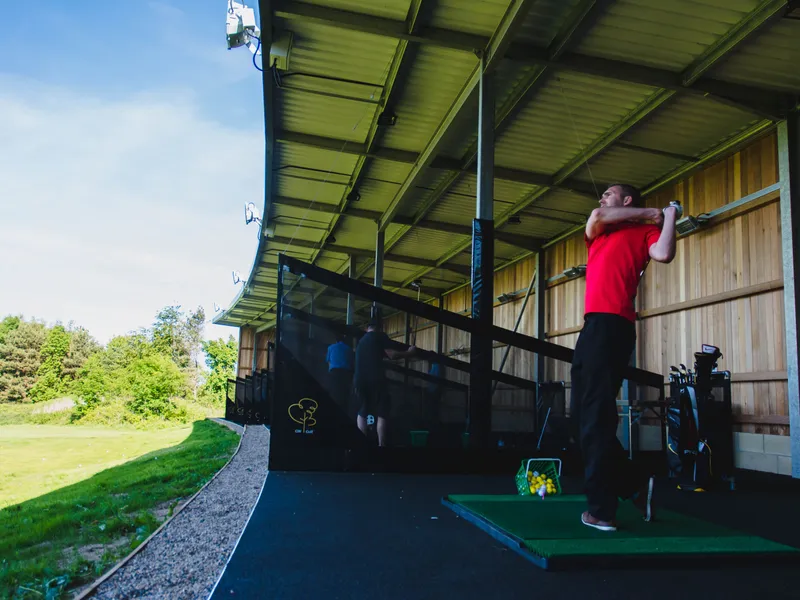Golfer in a red shirt finishing a swing at a covered driving range
