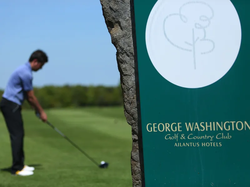 Golfer preparing to tee off beside a George Washington Golf and Country Club sign