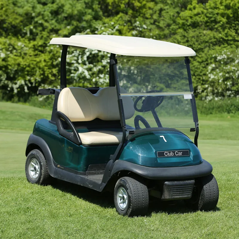 Green golf buggy parked on a manicured golf course beside leafy trees