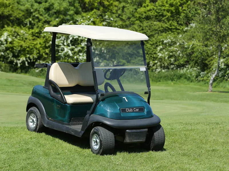 Green golf buggy parked on a manicured golf course beside leafy trees