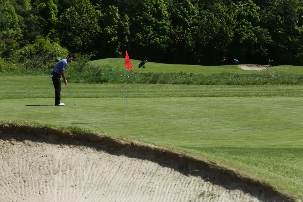 Golfer preparing a putt on a green beside a red flag and sand bunker