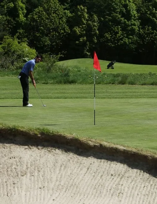 Golfer preparing a putt on a green beside a red flag and sand bunker