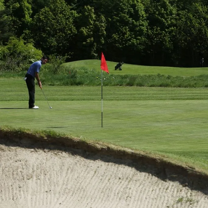 Golfer preparing a putt on a green beside a red flag and sand bunker