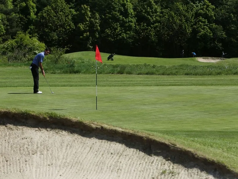 Golfer preparing a putt on a green beside a red flag and sand bunker