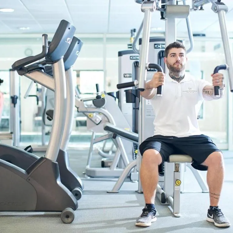 Tattooed man using a seated chest press machine in a bright modern gym