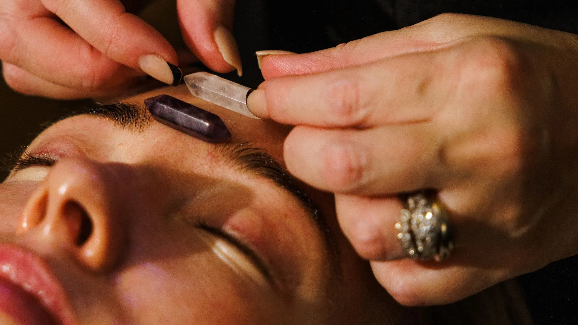 Close-up of a crystal healing treatment with amethyst and clear quartz placed on a person's forehead.