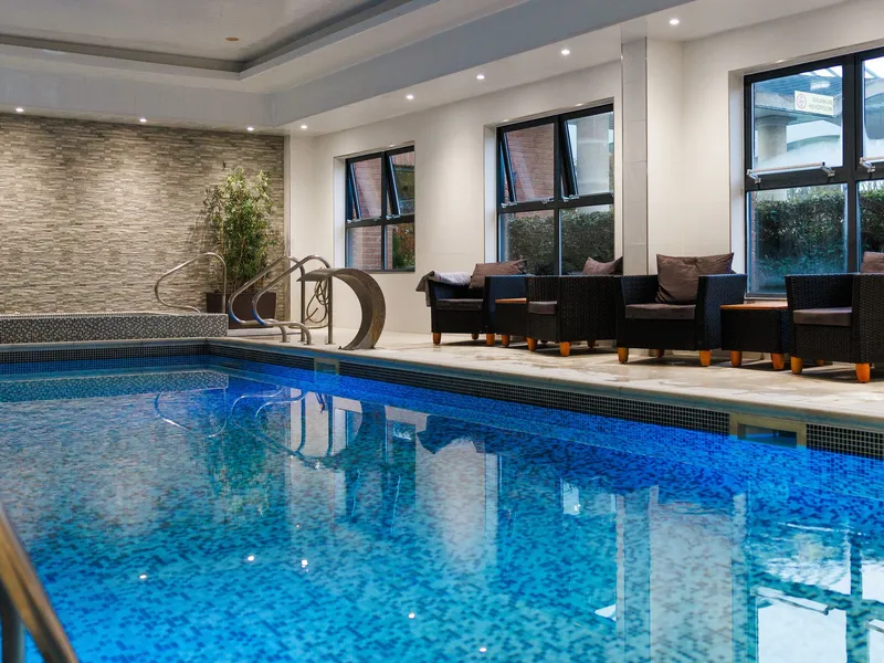 Modern indoor swimming pool with blue mosaic tiles, lounge chairs and large windows