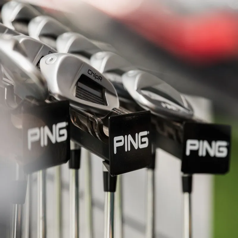 Close-up of Ping golf clubs arranged in a retail display rack.