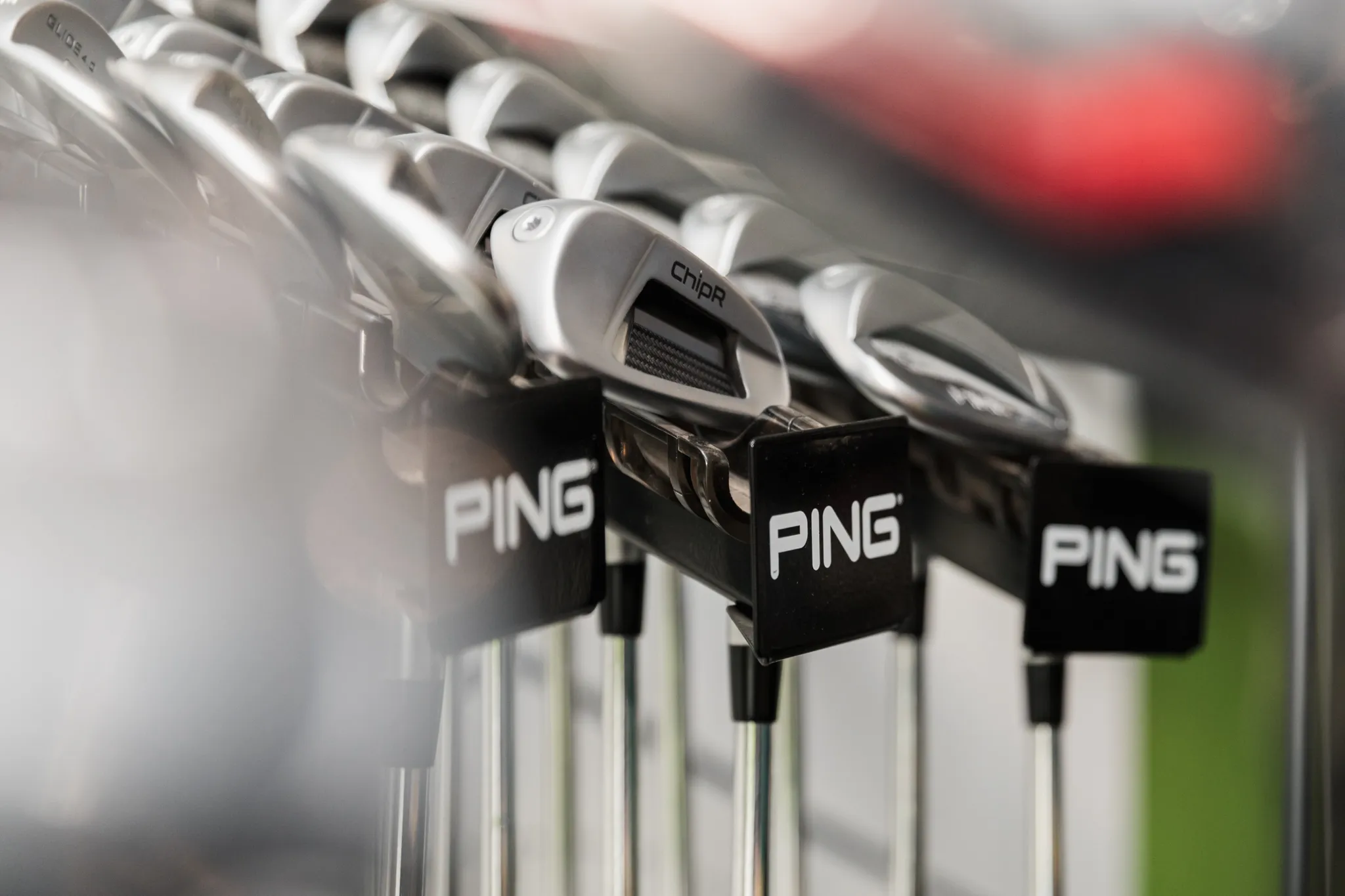 Close-up of Ping golf clubs arranged in a retail display rack.