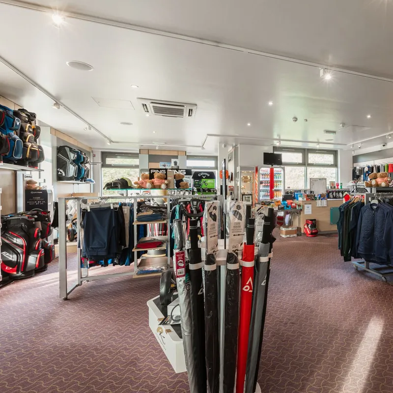 Brightly lit golf pro shop displaying golf bags, clothing, umbrellas, hats and accessories.