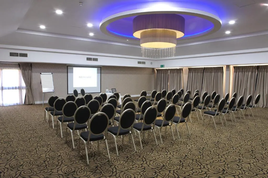 Hotel conference room with rows of black chairs facing a projection screen and flip chart.