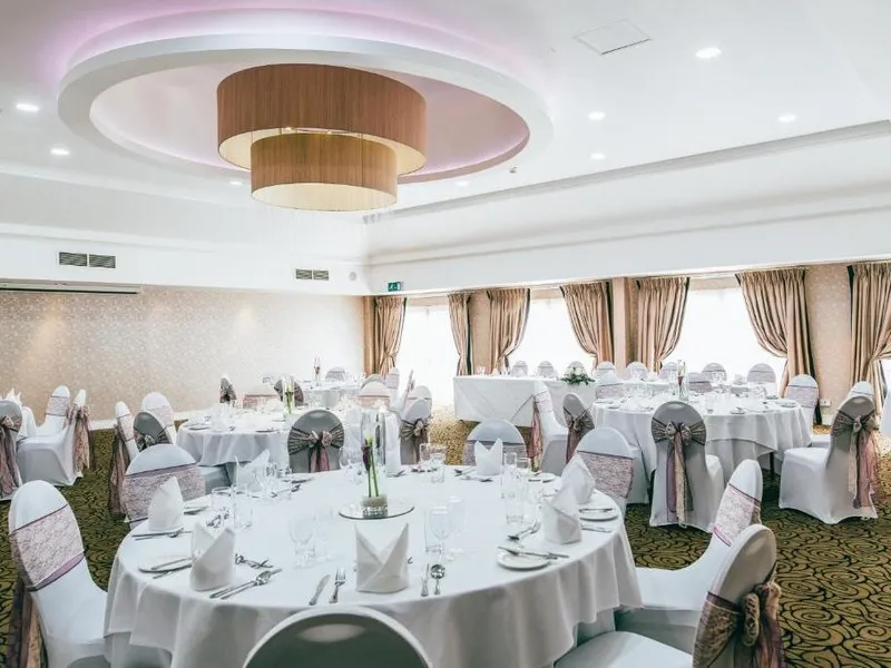 Elegant banquet hall set for a formal wedding reception with round tables and decorated chairs.