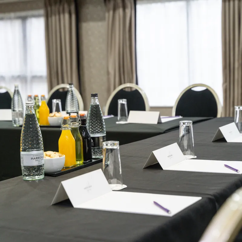 Conference room arranged with black-clothed tables, bottled water, juice, glasses, notepads and pens.