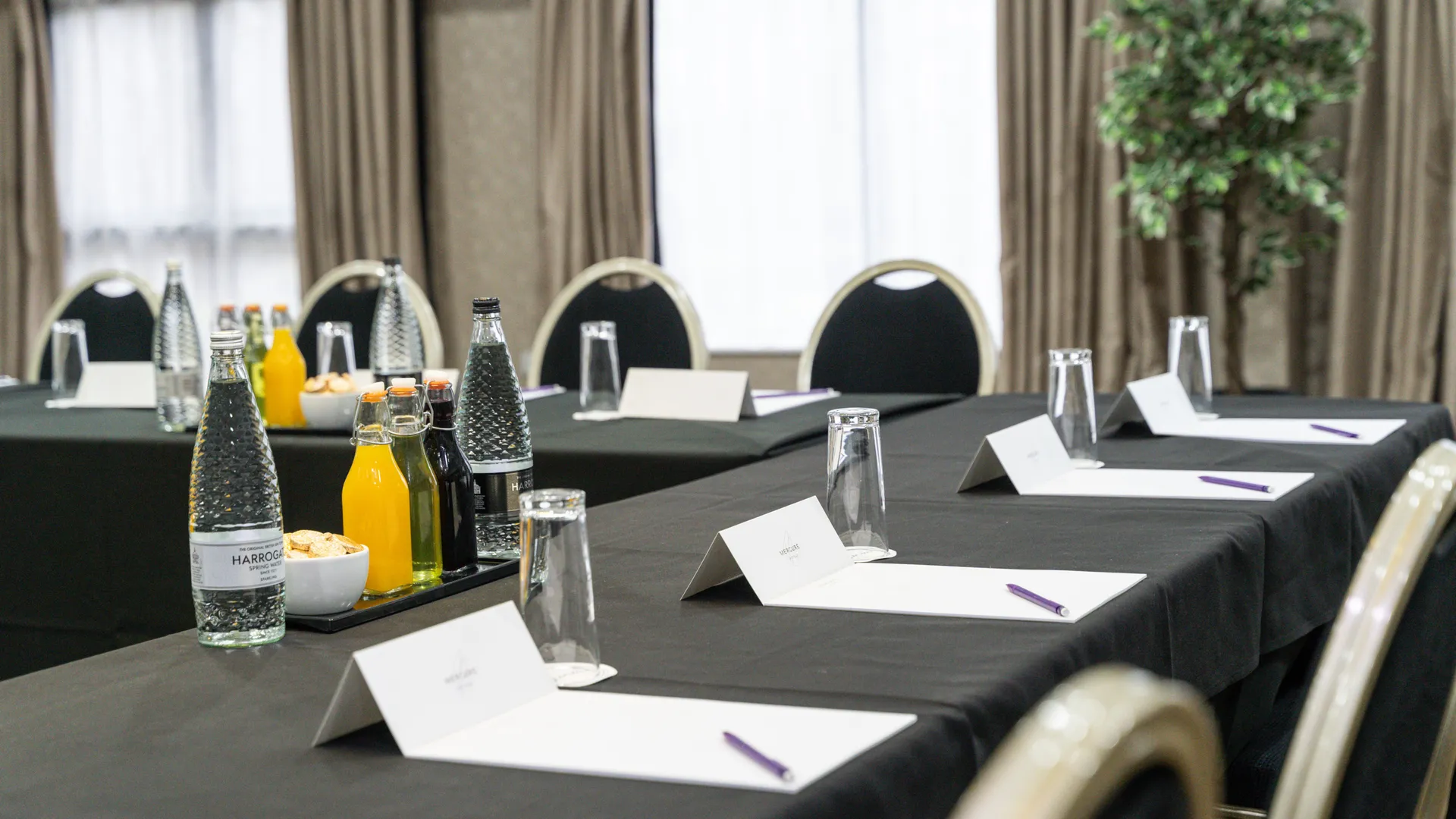 Conference room arranged with black-clothed tables, bottled water, juice, glasses, notepads and pens.