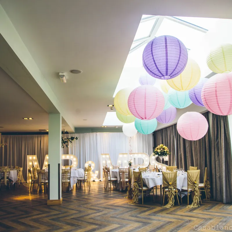 Elegant wedding reception room decorated with pastel paper lanterns, gold-covered chairs and illuminated MR and MRS letters.