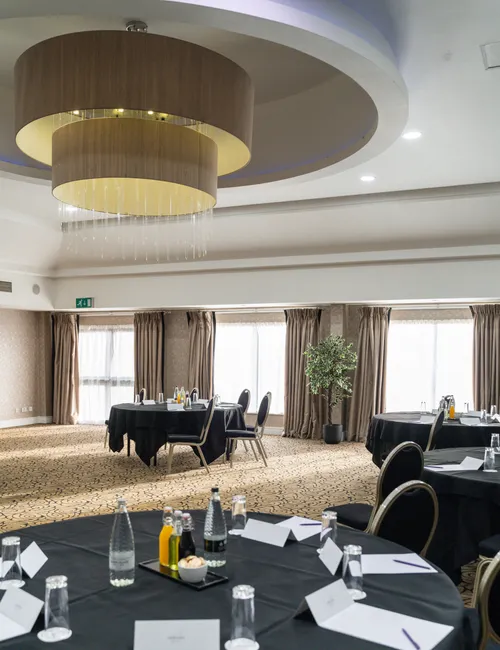 Elegant conference room with round tables, black tablecloths and a large layered chandelier.