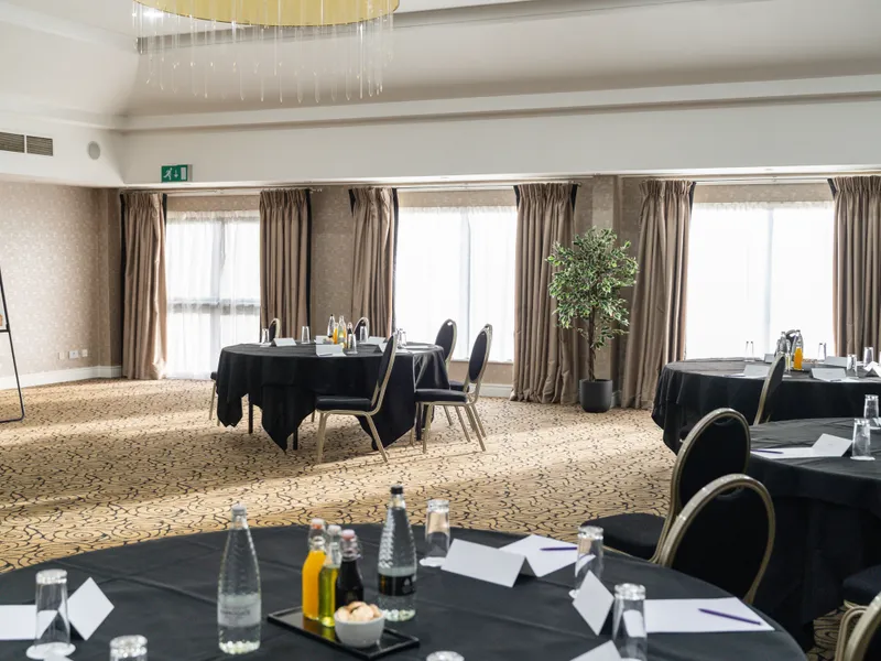 Elegant conference room with round tables, black tablecloths and a large layered chandelier.
