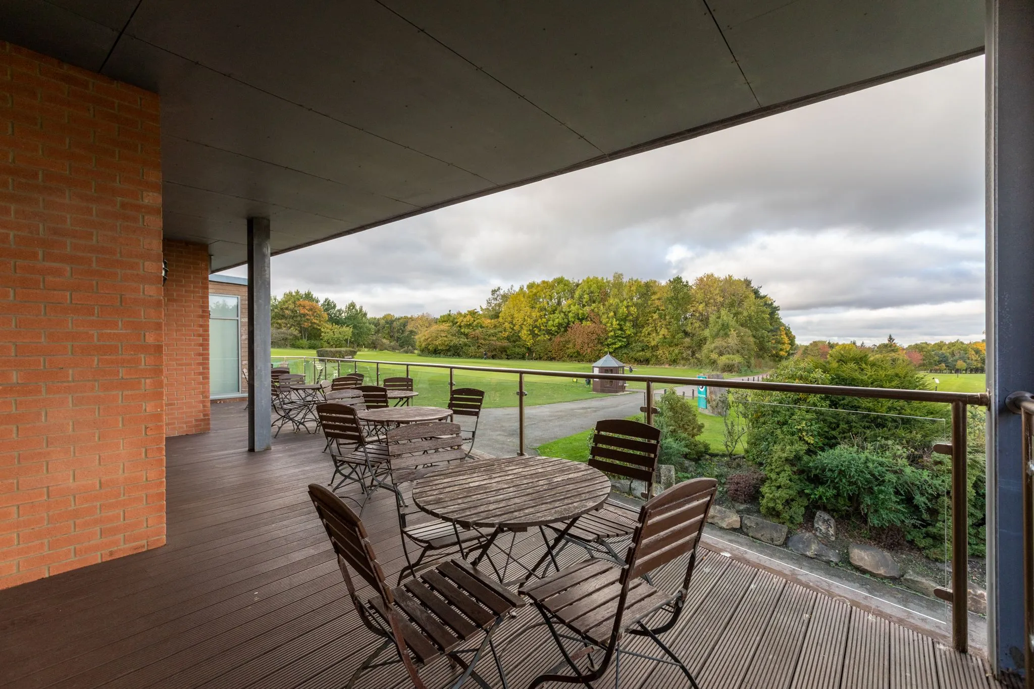 Covered terrace with wooden tables and folding chairs overlooking a green parkland landscape.