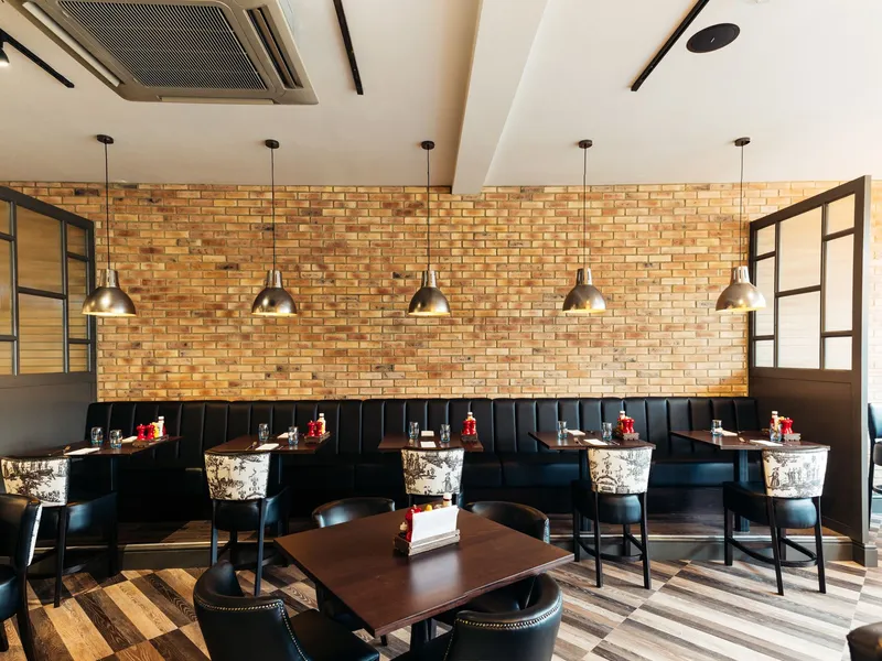 Stylish restaurant dining area with exposed brick walls, black banquette seating and pendant lights.