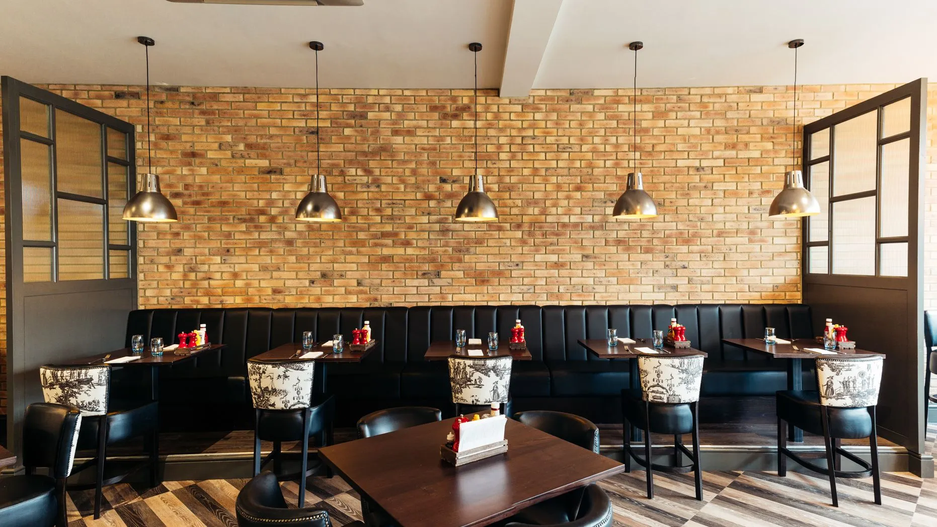 Stylish restaurant dining area with exposed brick walls, black banquette seating and pendant lights.