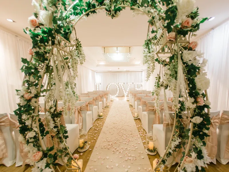 Elegant wedding ceremony room with a flower-covered arch, petal-strewn aisle and illuminated LOVE letters.