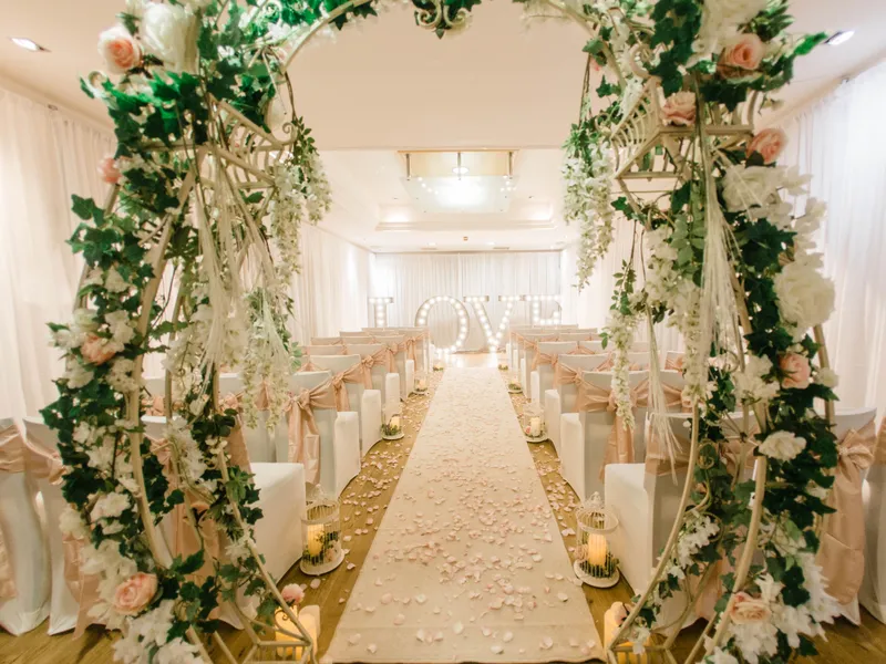 Elegant wedding ceremony room with a flower-covered arch, petal-strewn aisle and illuminated LOVE letters.