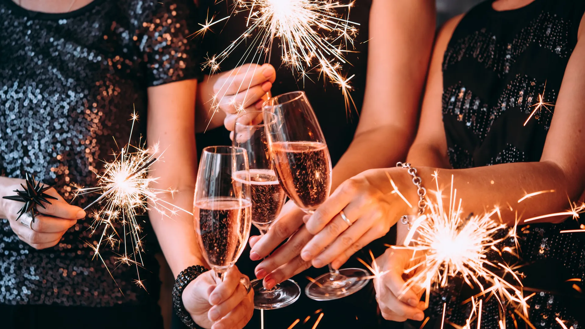 Women in black sequinned dresses holding champagne flutes and sparklers at a celebration