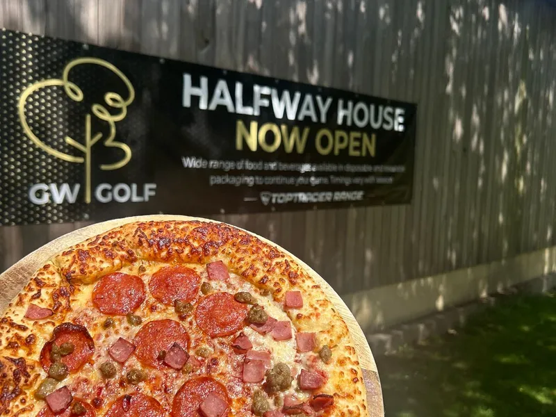 Pepperoni, ham and sausage pizza held in front of a GW Golf Halfway House sign.