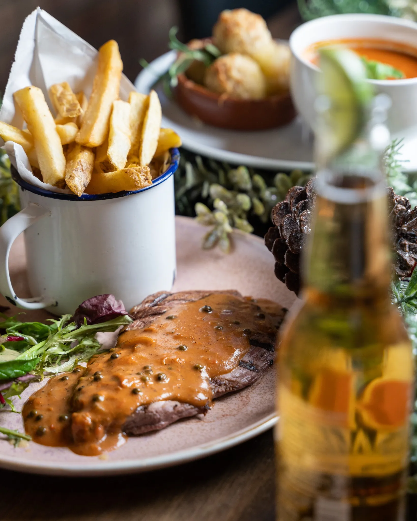 Steak topped with peppercorn sauce, served with chips and a side salad beside a glass of beer.