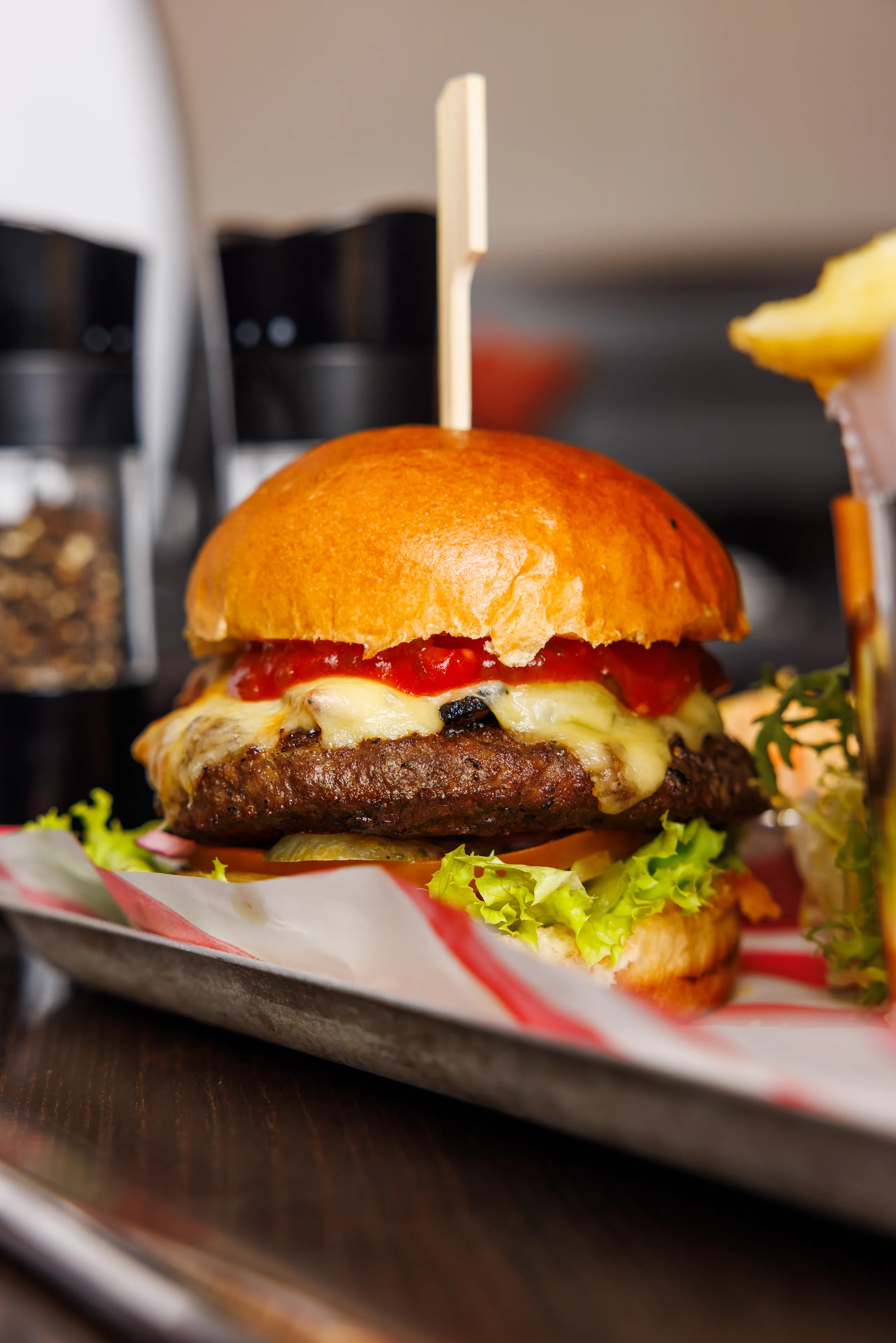 Gourmet beef cheeseburger with melted cheese, tomato sauce, lettuce and pickles on a tray