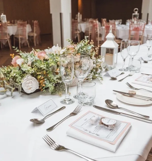 Elegant wedding reception table with pastel floral centrepiece, white lantern and formal place settings.