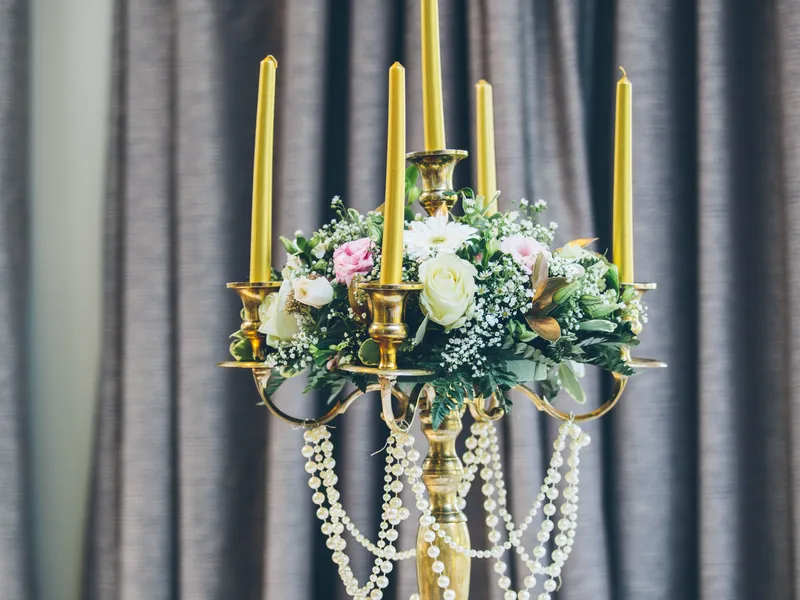 Elegant gold candelabra centrepiece with yellow taper candles, pastel flowers and pearl garlands on a formally set dining table.