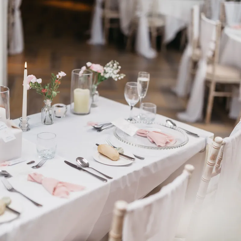 Elegant wedding reception table with blush pink napkins, floral arrangements, candles and white chairs.