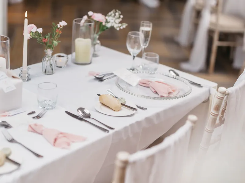 Elegant wedding reception table with blush pink napkins, floral arrangements, candles and white chairs.