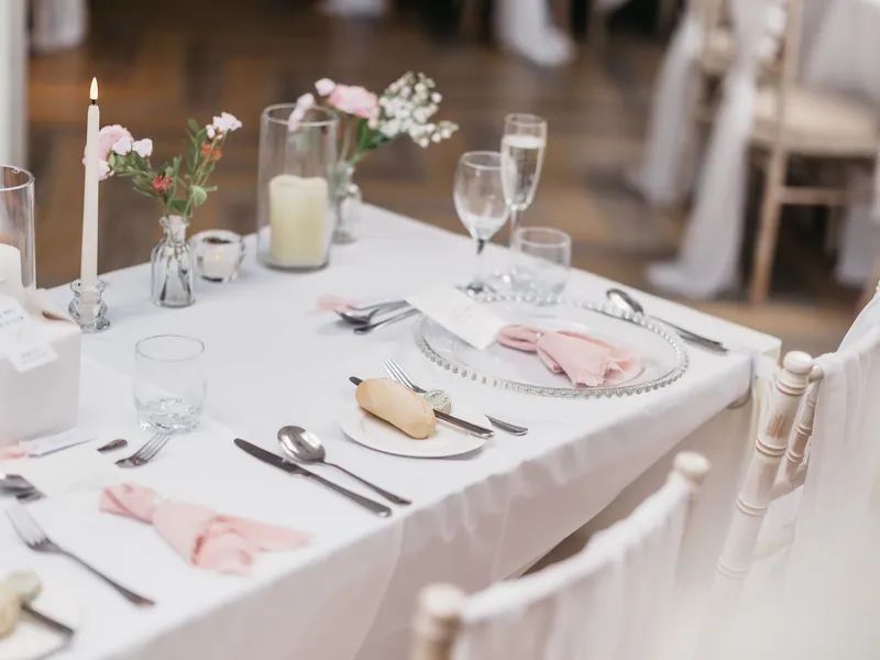 Elegant wedding reception table with blush pink napkins, floral arrangements, candles and white chairs.