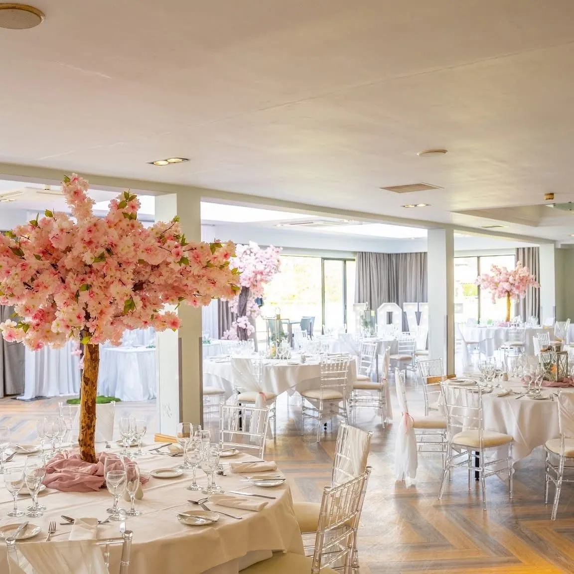 Elegant wedding reception in an orangery with pink blossom centrepieces and white table settings