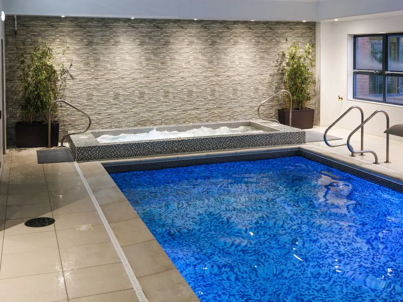 Indoor swimming pool with blue mosaic tiles, hot tub and potted bamboo plants