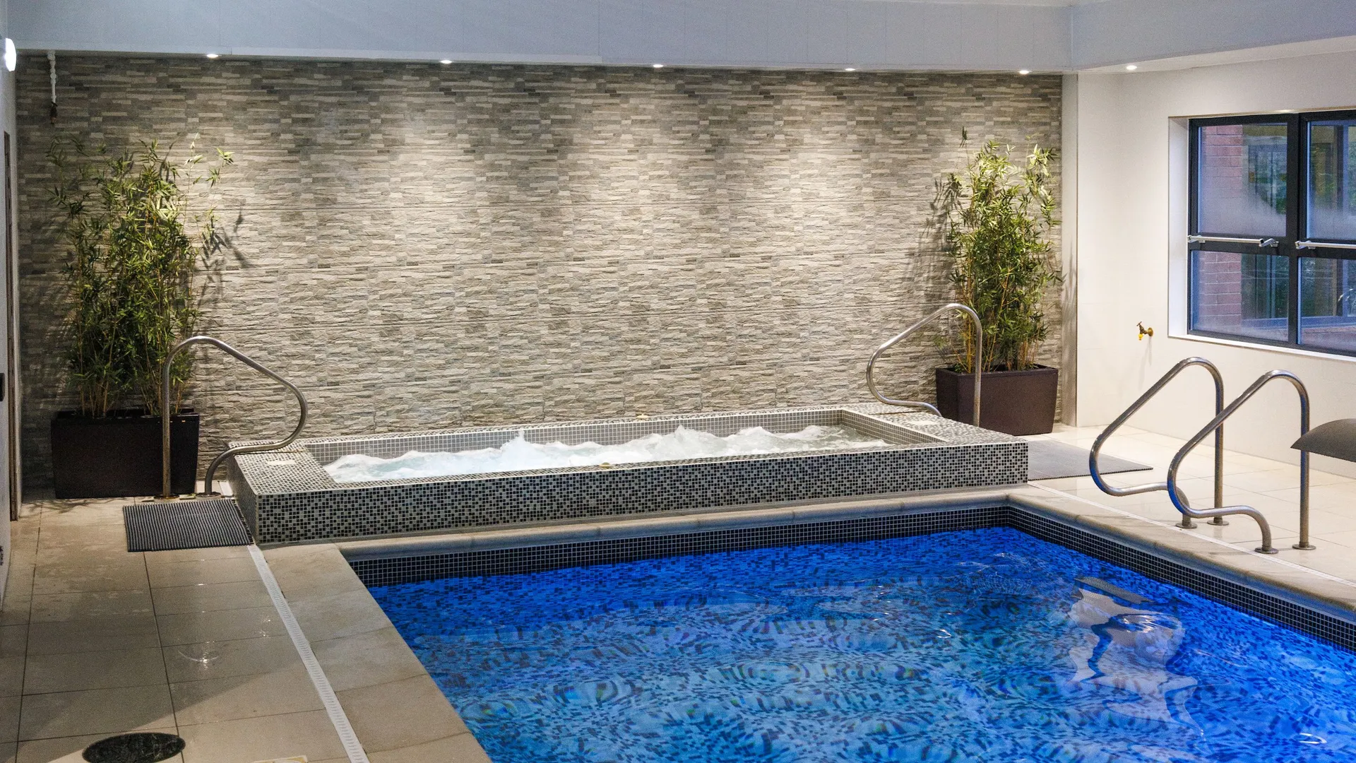 Indoor swimming pool with blue mosaic tiles, hot tub and potted bamboo plants