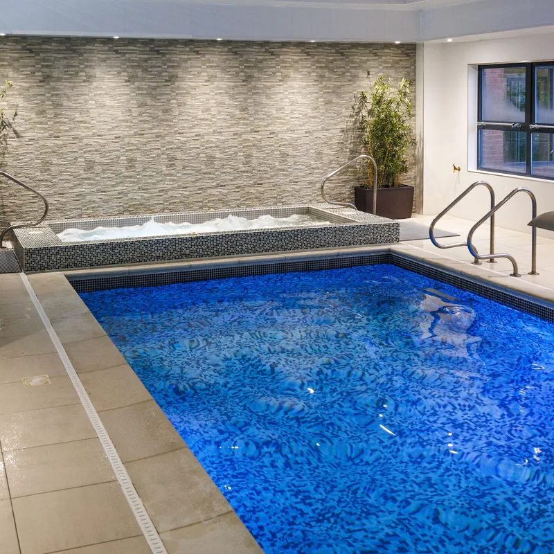Indoor swimming pool with blue mosaic tiles, hot tub and potted bamboo plants