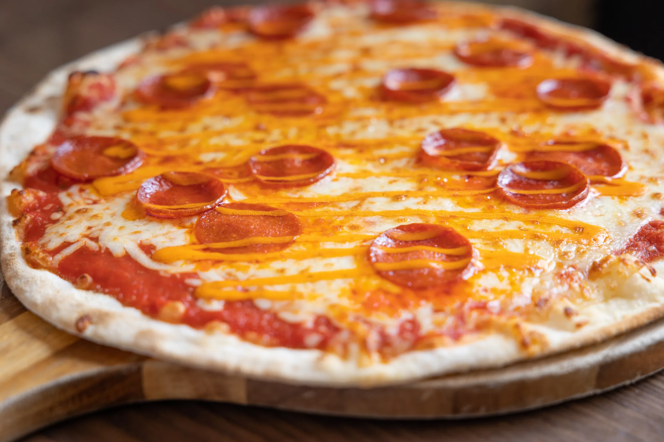 Pepperoni pizza with melted cheese and orange sauce drizzle on a wooden board