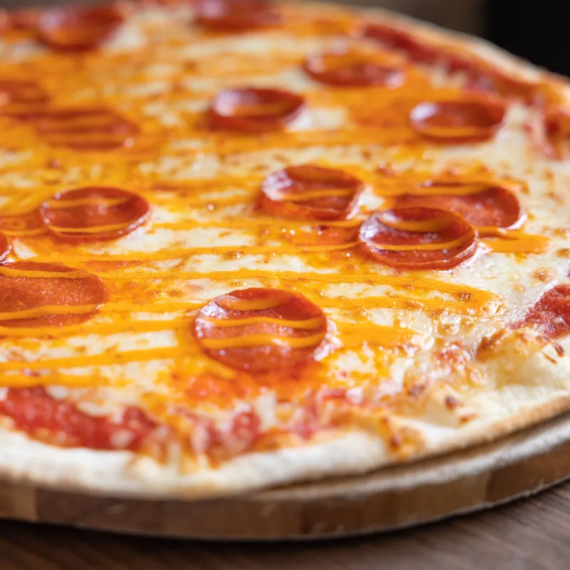 Pepperoni pizza with melted cheese and orange sauce drizzle on a wooden board