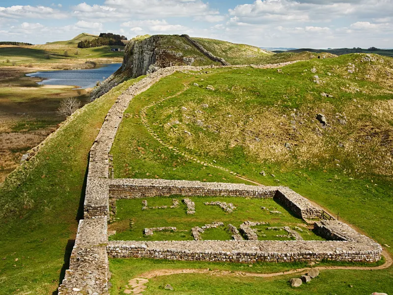 Hadrian's Wall winding across green hills beside a lake in northern England